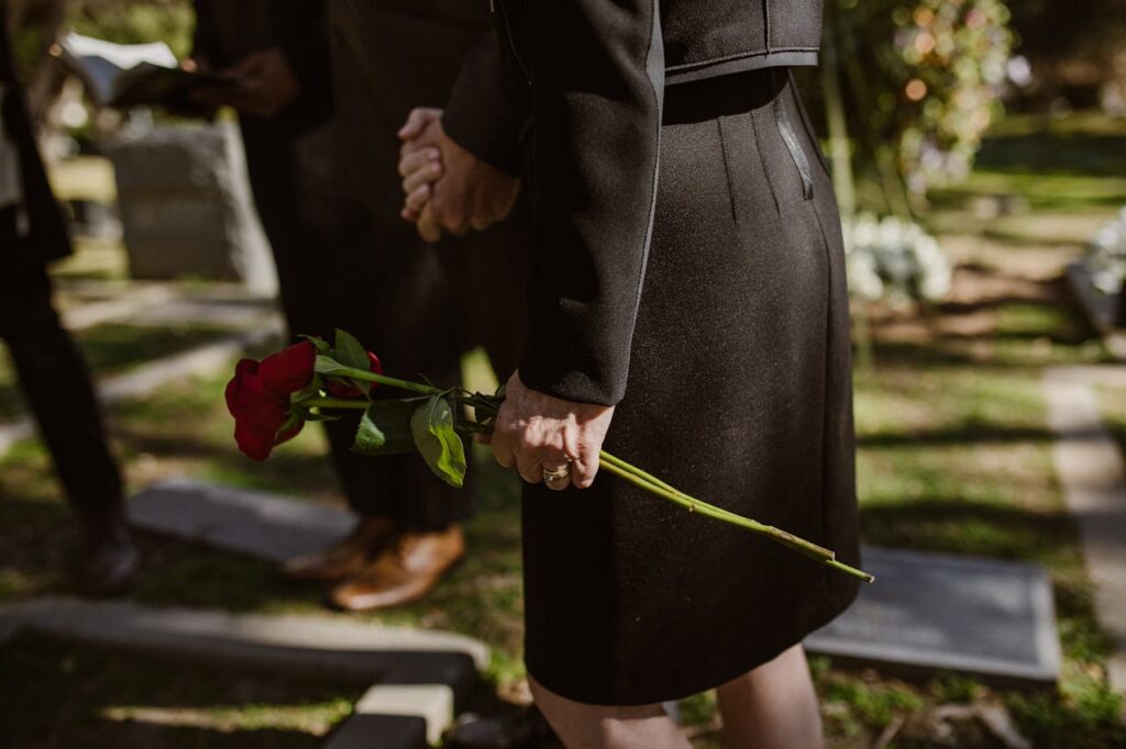Close-up of a person in black attire holding a red rose at a cemetery.