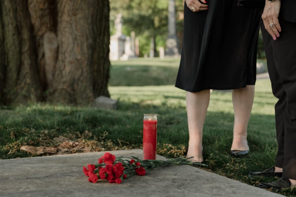 A solemn scene at a cemetery with a red candle and flowers, symbolizing remembrance.